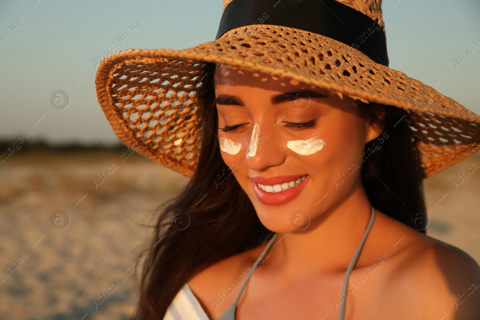 Photo of Happy young woman with sun protection cream on face at beach