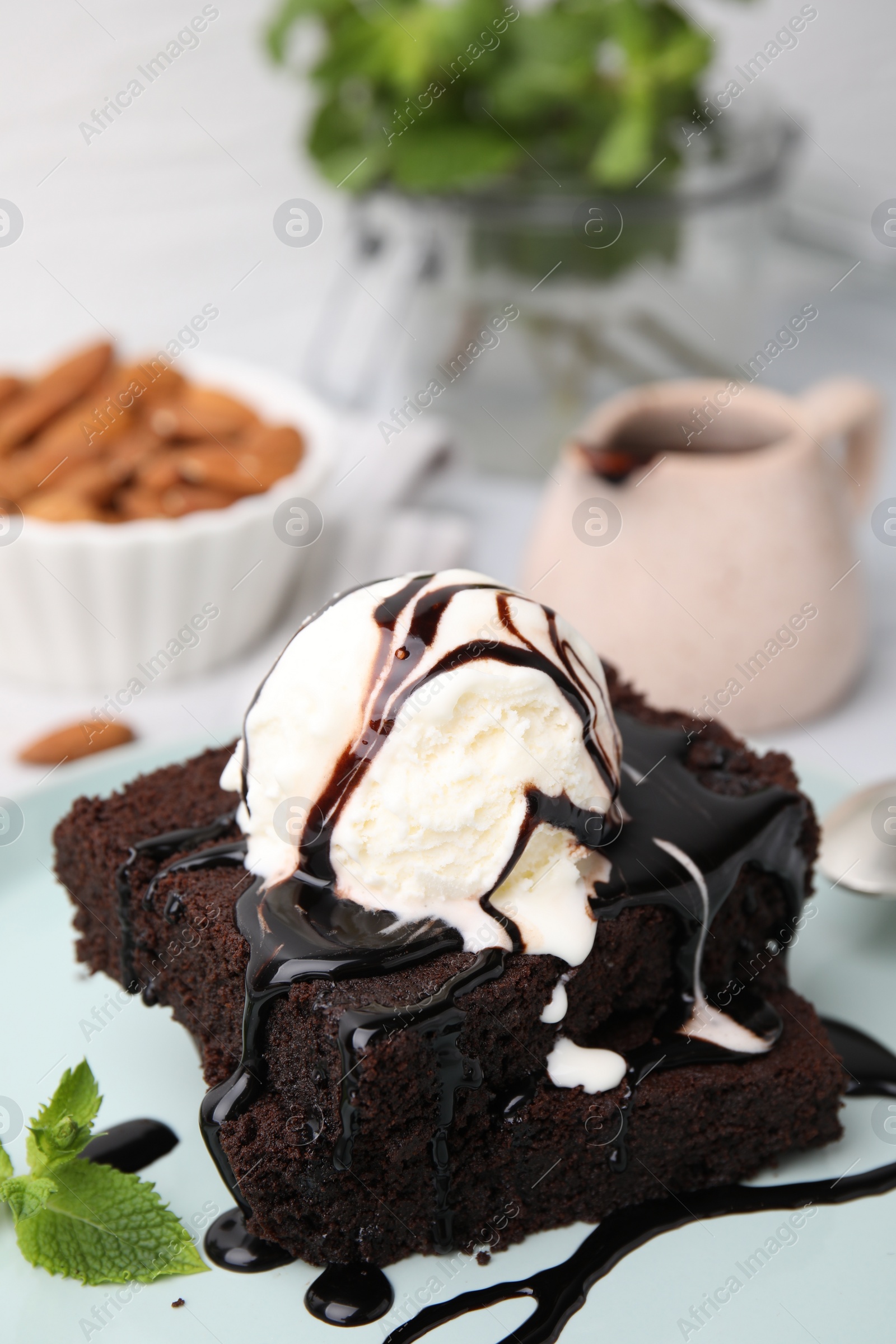 Photo of Tasty brownies served with ice cream and chocolate sauce on plate, closeup