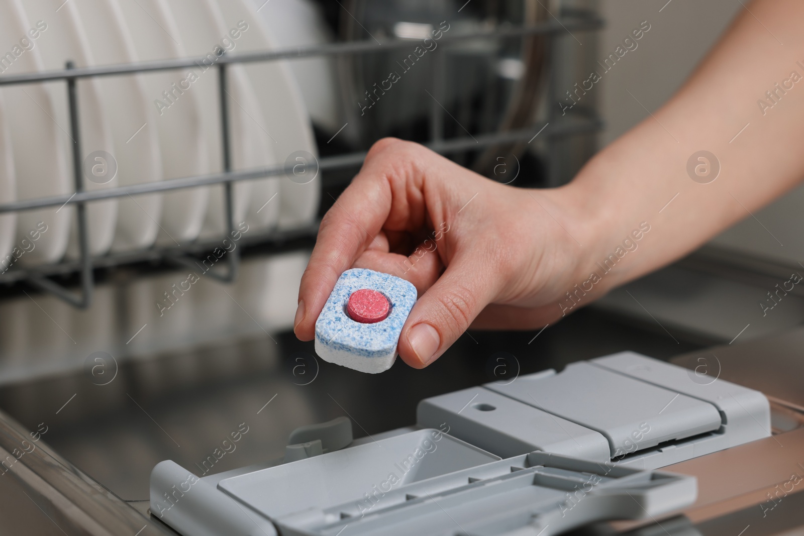 Photo of Woman putting detergent tablet into open dishwasher, closeup