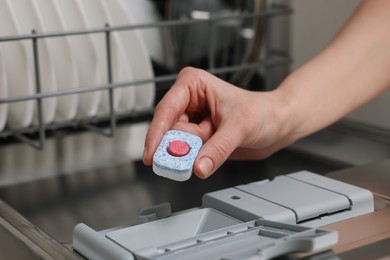 Photo of Woman putting detergent tablet into open dishwasher, closeup