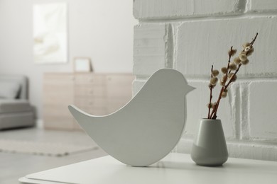 Photo of Bird shaped night lamp and pussy willow twigs on white table in child's room