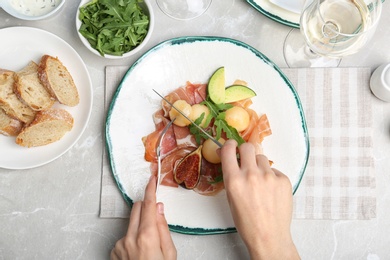 Woman cutting melon and prosciutto  appetizer at table, top view