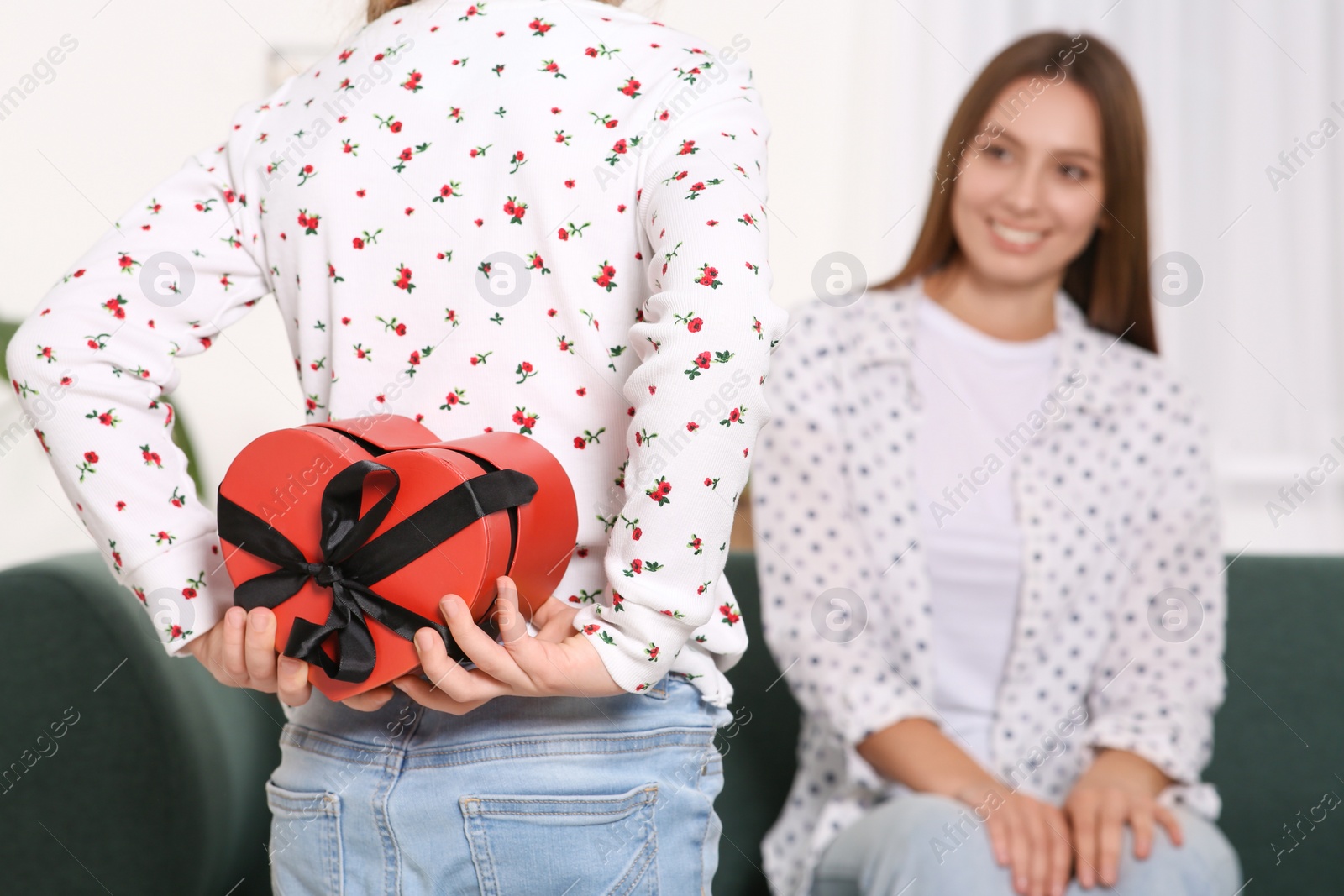 Photo of Little girl presenting her mother with gift on sofa at home