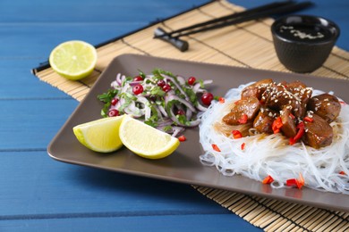 Photo of Pieces of soy sauce chicken with noodle, salad and lime served on blue wooden table, closeup