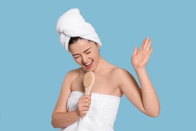 Photo of Emotional woman in towels singing into brush on light blue background. Spa treatment