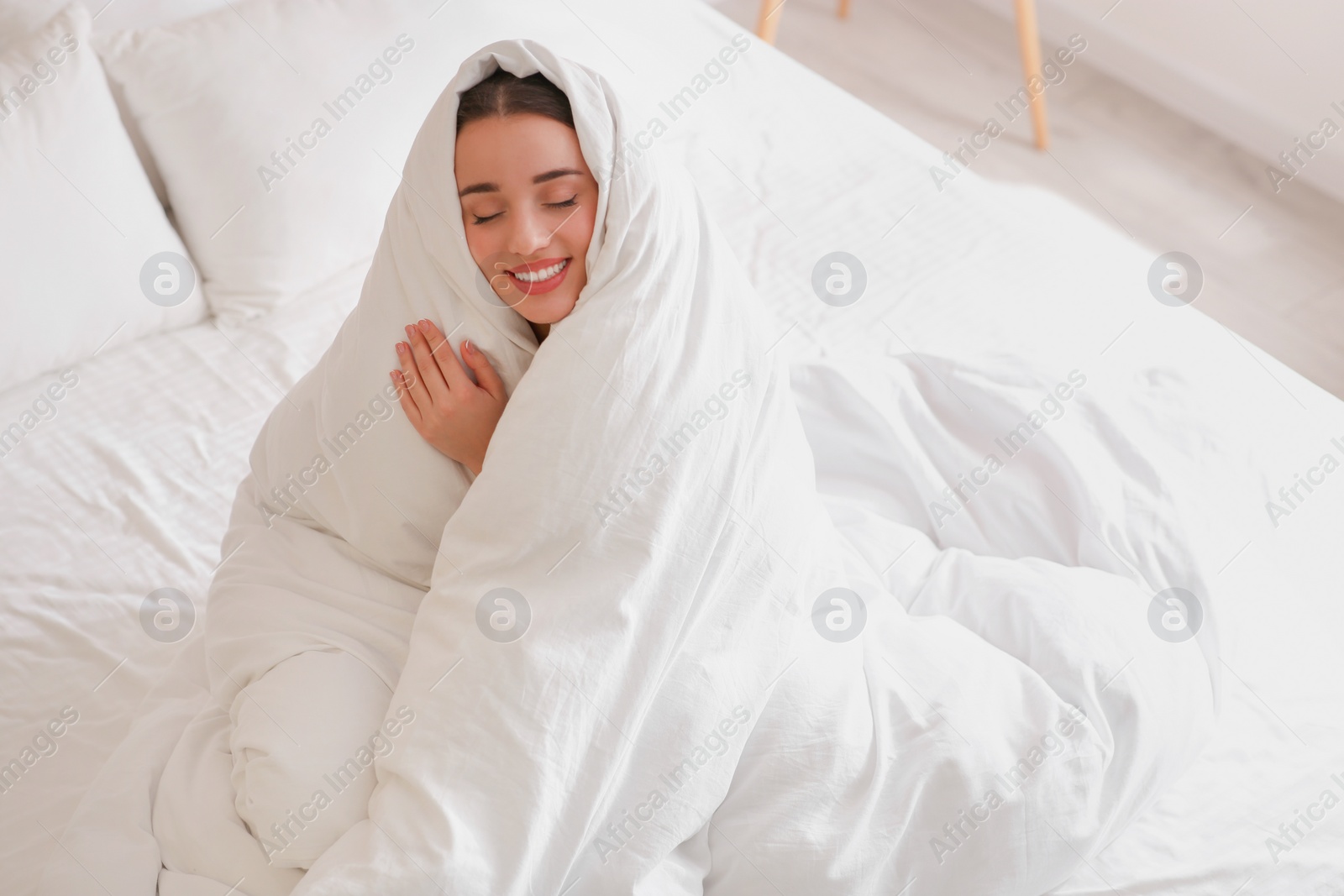 Photo of Beautiful young woman wrapped with soft blanket on bed at home