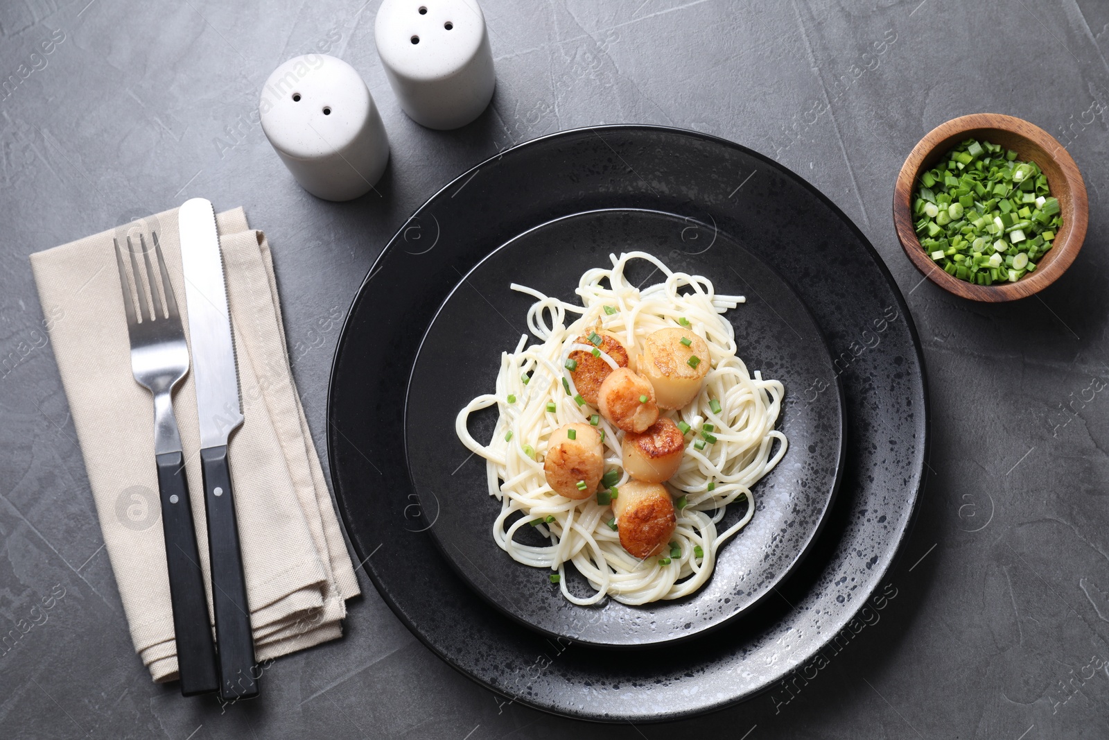 Photo of Delicious scallop pasta with green onion served on grey table, flat lay