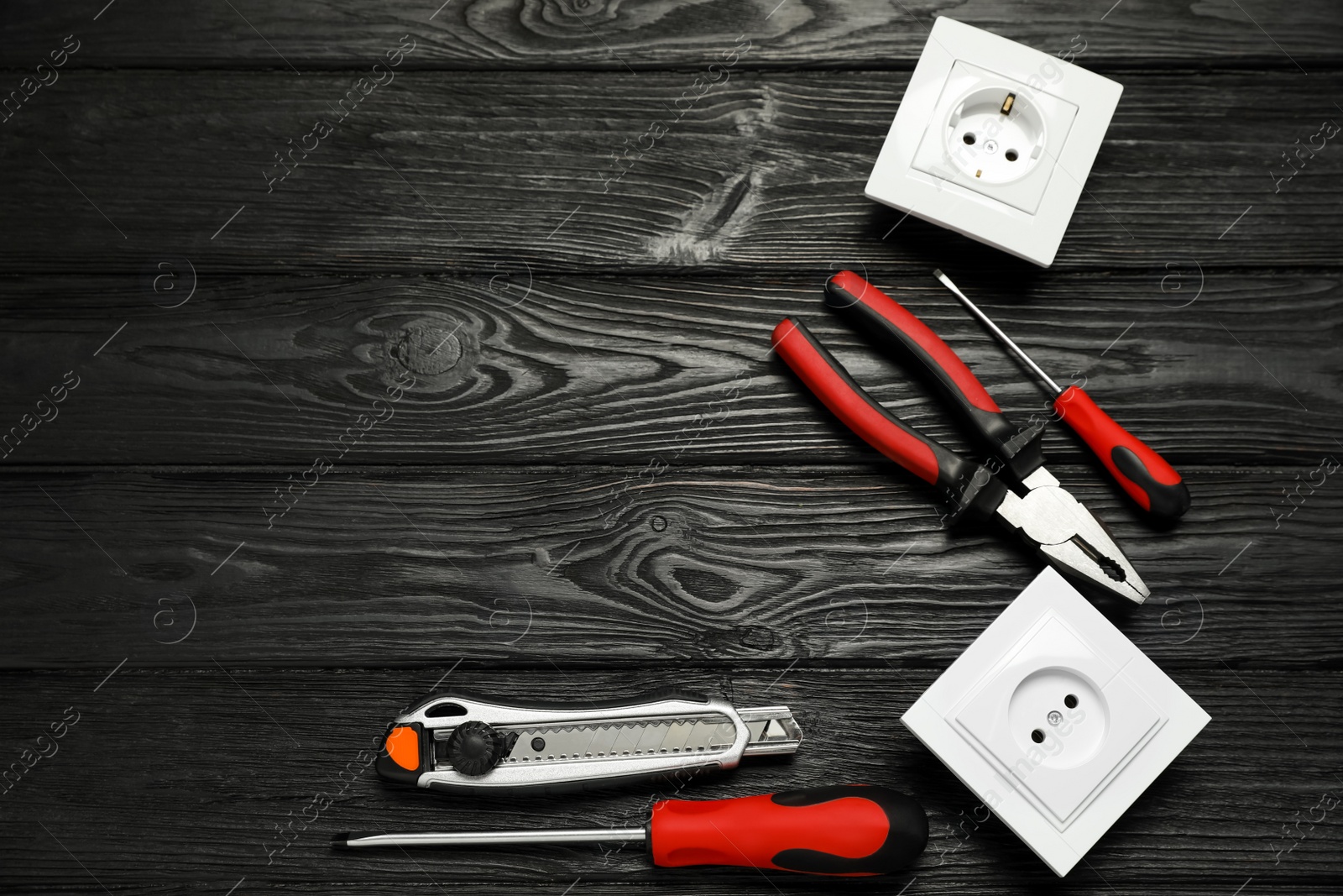 Photo of Set of electrician's tools and power sockets on black wooden table, flat lay. Space for text