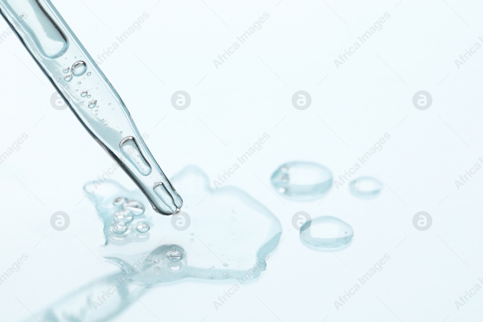 Photo of Glass pipette and transparent liquid on light background, closeup. Space for text