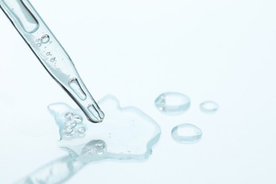 Photo of Glass pipette and transparent liquid on light background, closeup. Space for text