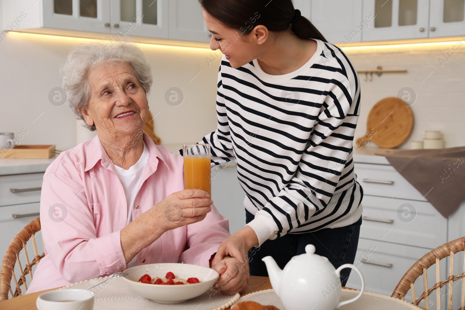 Photo of Young caregiver serving breakfast for senior woman at table in kitchen. Home care service