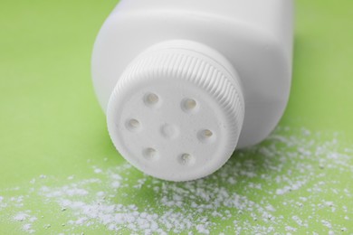 Photo of Bottle and scattered dusting powder on light green background, closeup. Baby cosmetic product