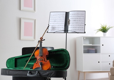 Photo of Violin, case and note stand with music sheets in room