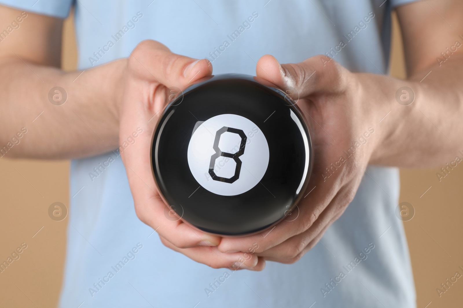 Photo of Man holding magic eight ball on light brown background, closeup