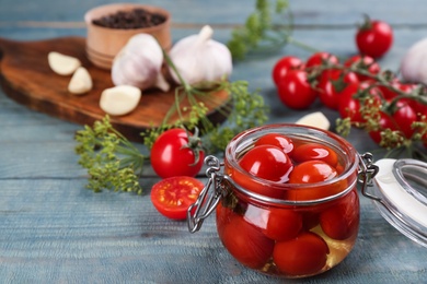 Glass jar of pickled cherry tomatoes on light blue wooden table. Space for text