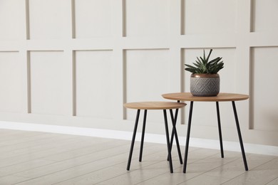 Photo of Tables with potted houseplant near empty wall indoors. Space for design