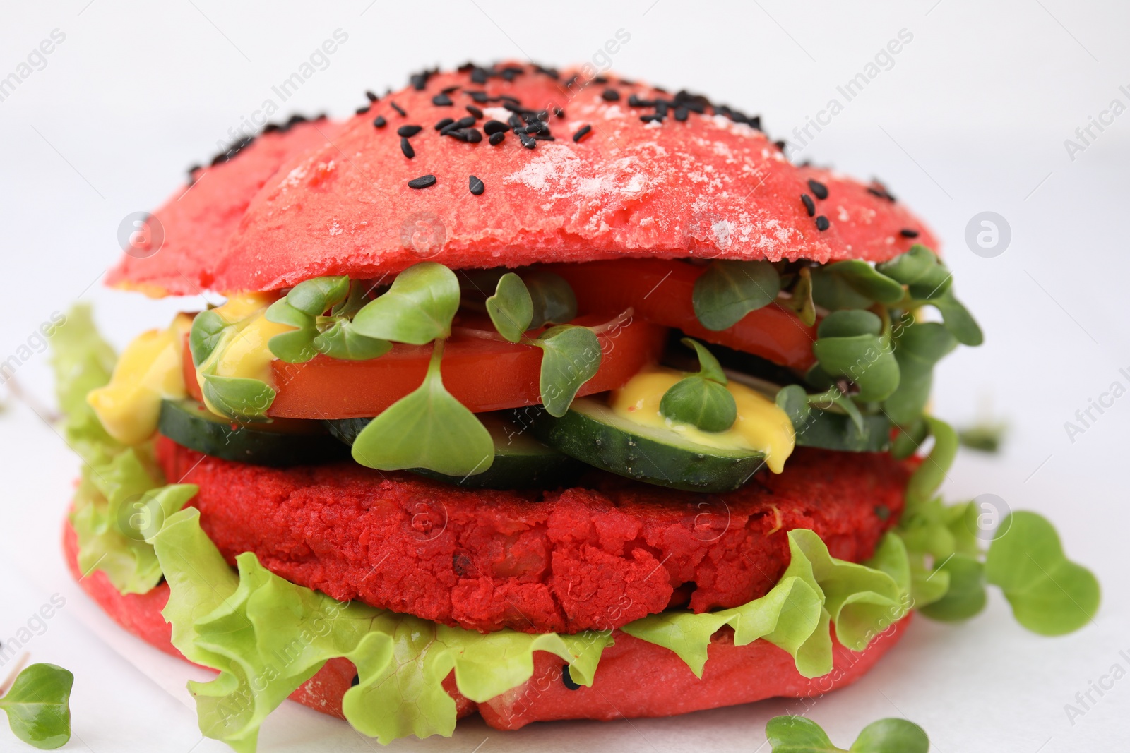 Photo of Tasty pink vegan burger with vegetables, patty and microgreens on white background, closeup