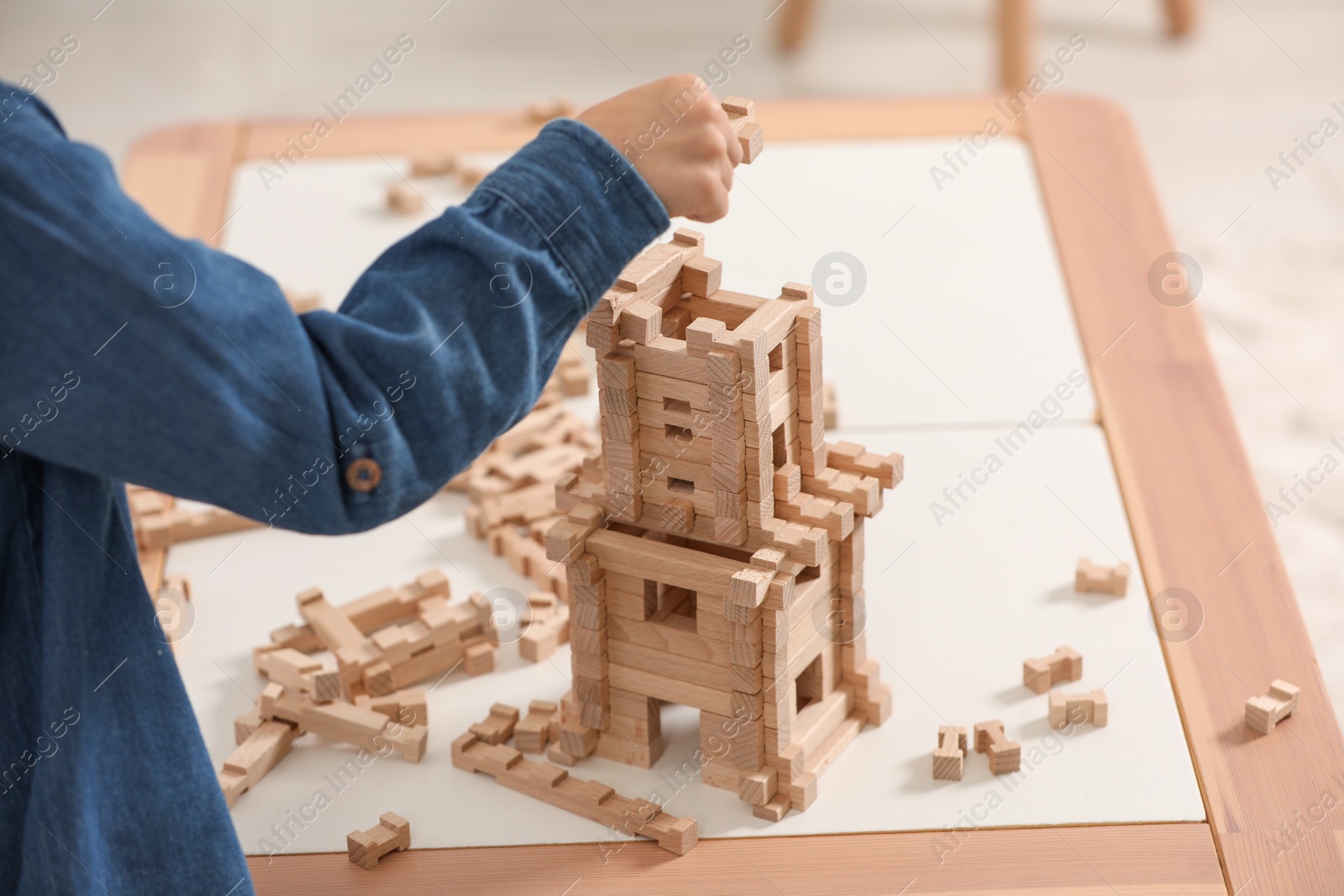 Photo of Little boy playing with wooden tower at table indoors, closeup. Child's toy