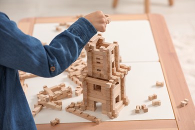 Little boy playing with wooden tower at table indoors, closeup. Child's toy