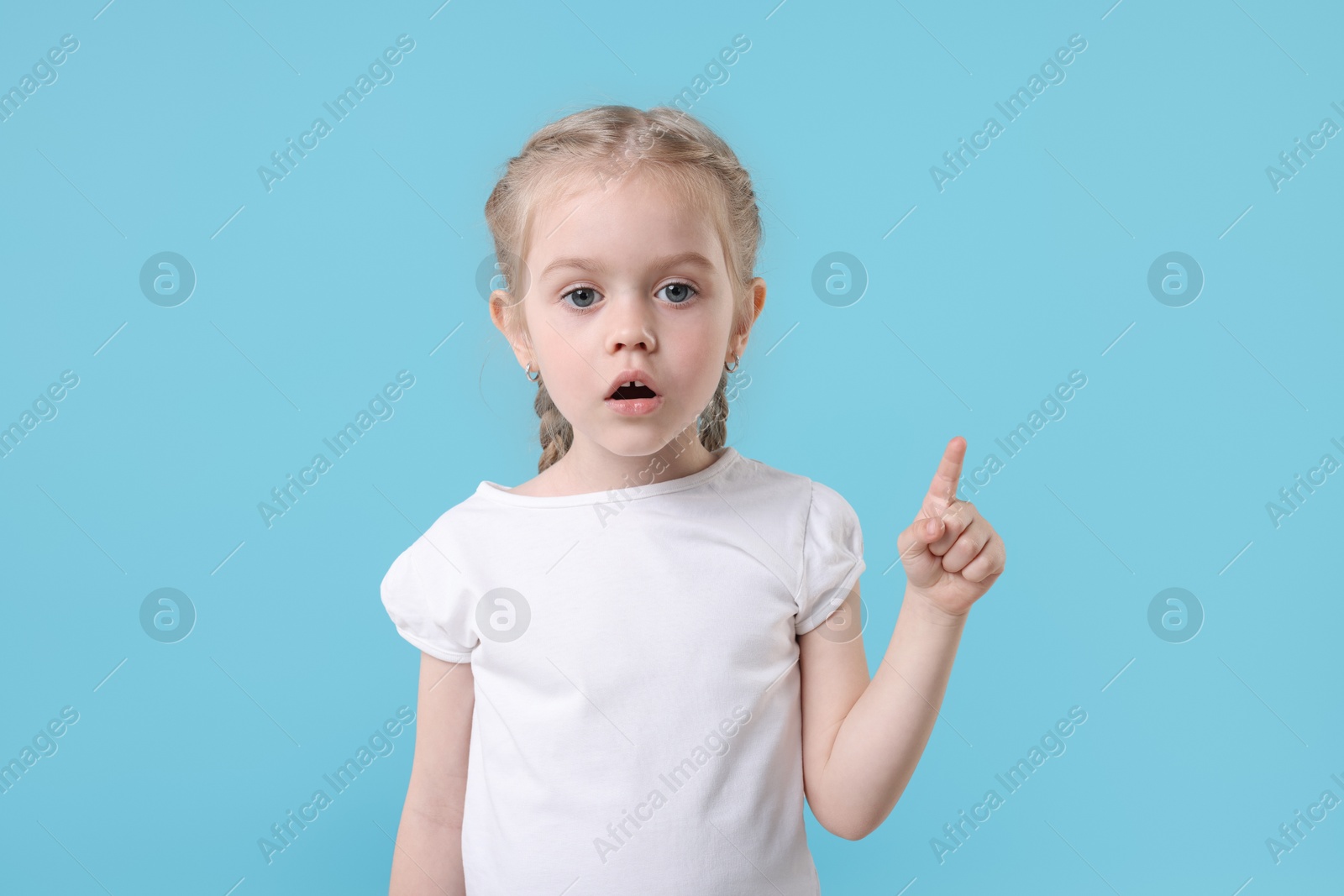 Photo of Cute little girl pointing at something on light blue background