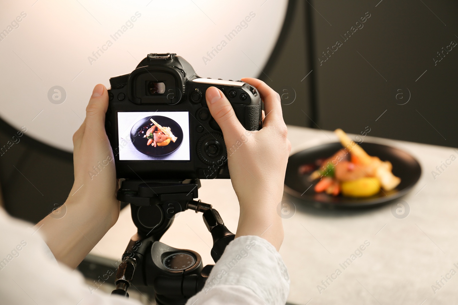 Photo of Woman taking picture of dish with chicken, parsnip and strawberries on grey table in professional photo studio, closeup. Food stylist