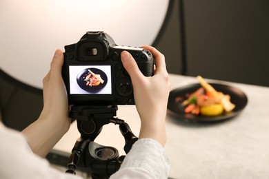 Photo of Woman taking picture of dish with chicken, parsnip and strawberries on grey table in professional photo studio, closeup. Food stylist