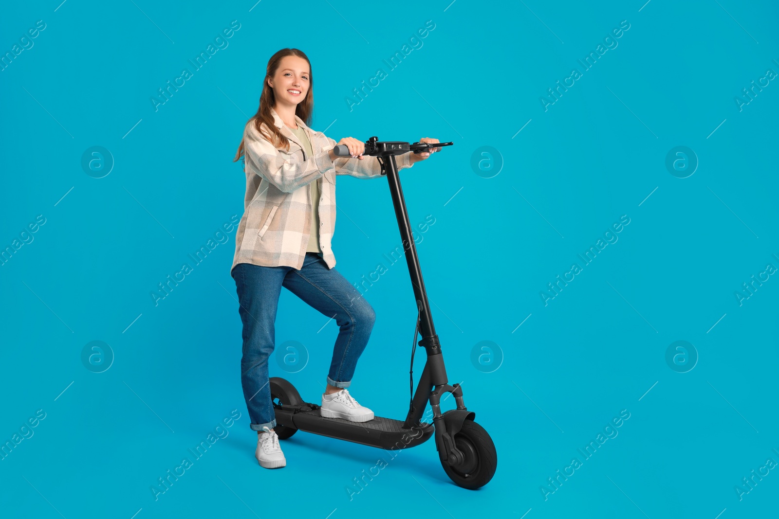 Photo of Happy woman with modern electric kick scooter on light blue background