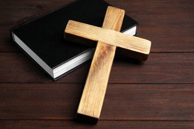 Photo of Christian cross and Bible on wooden background, closeup. Religion concept