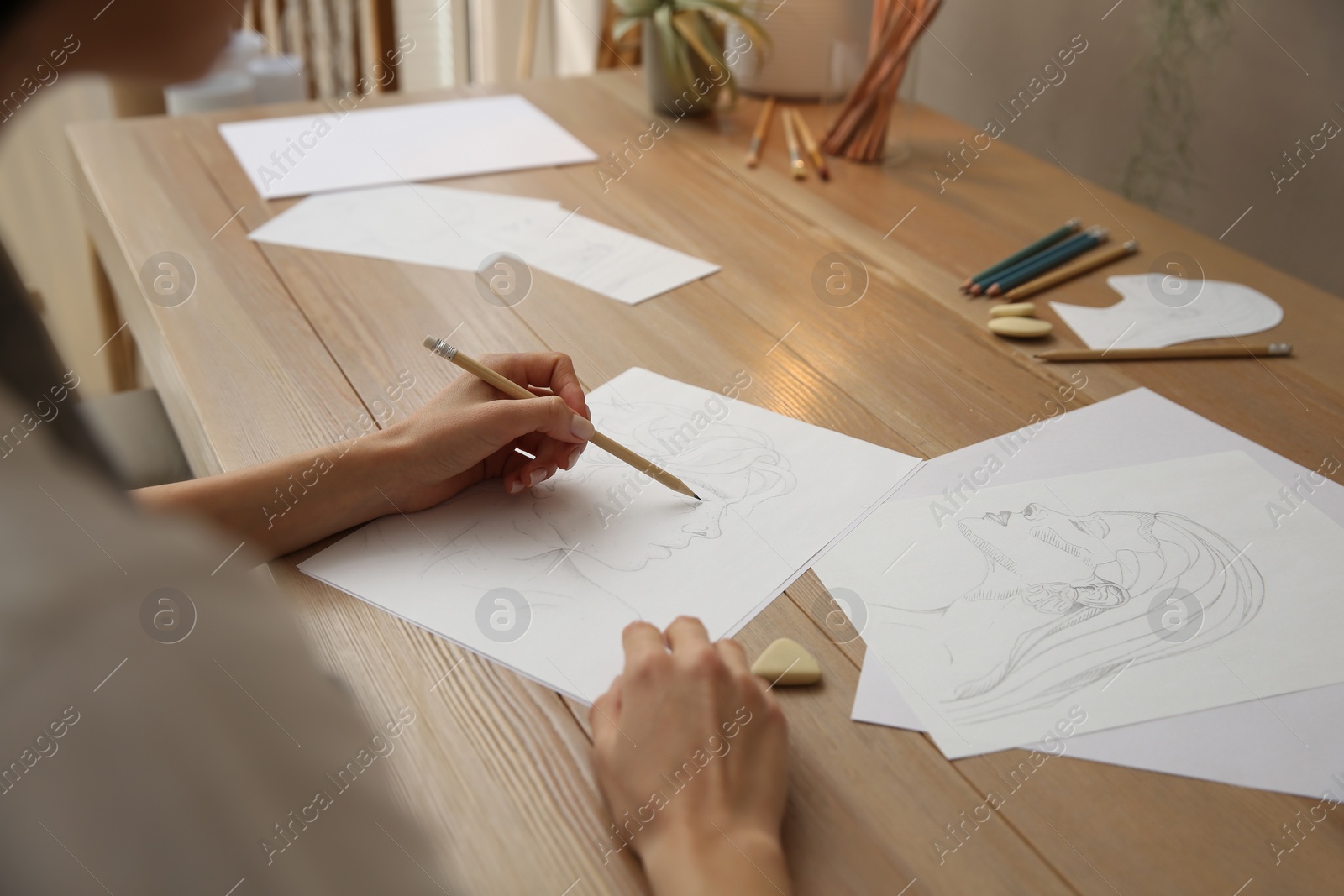 Photo of Young woman drawing male portrait at table indoors, closeup