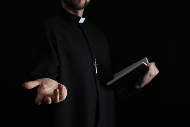 Photo of Priest with Bible praying on dark background, closeup