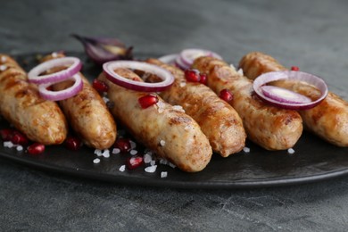 Photo of Tasty grilled sausages with onion rings and pomegranate seeds served on grey table, closeup