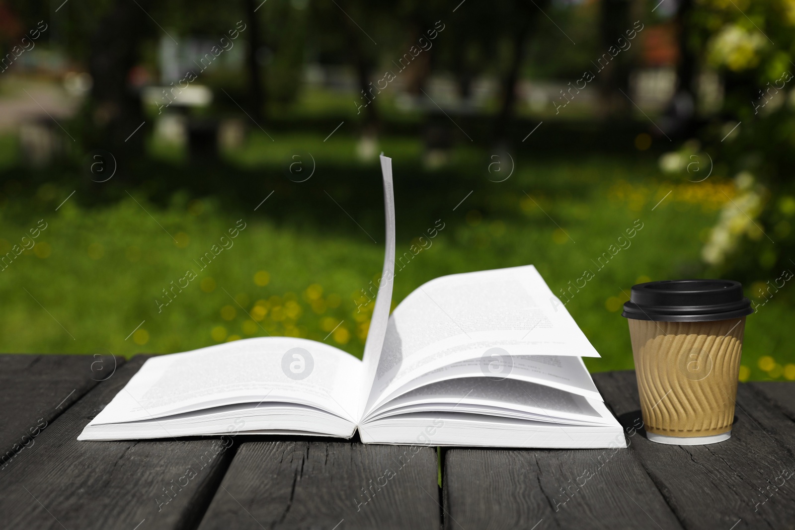 Photo of Open book and paper coffee cup on wooden table outdoors