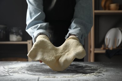 Photo of Woman tossing pizza dough at table in kitchen, closeup