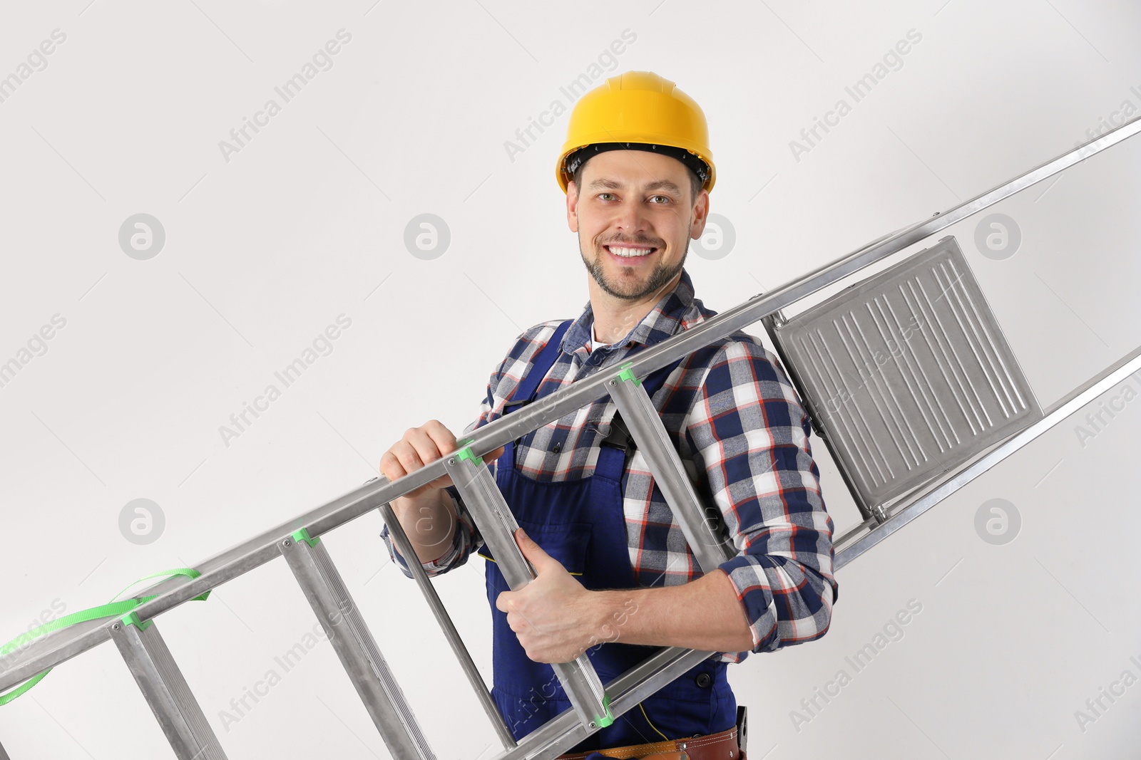 Photo of Handsome working man in hard hat holding ladder against white background