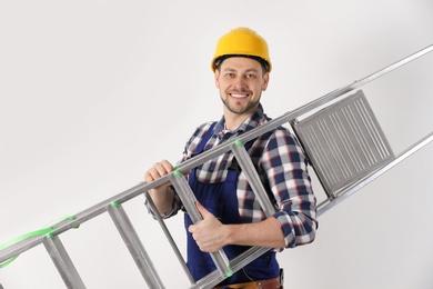 Handsome working man in hard hat holding ladder against white background