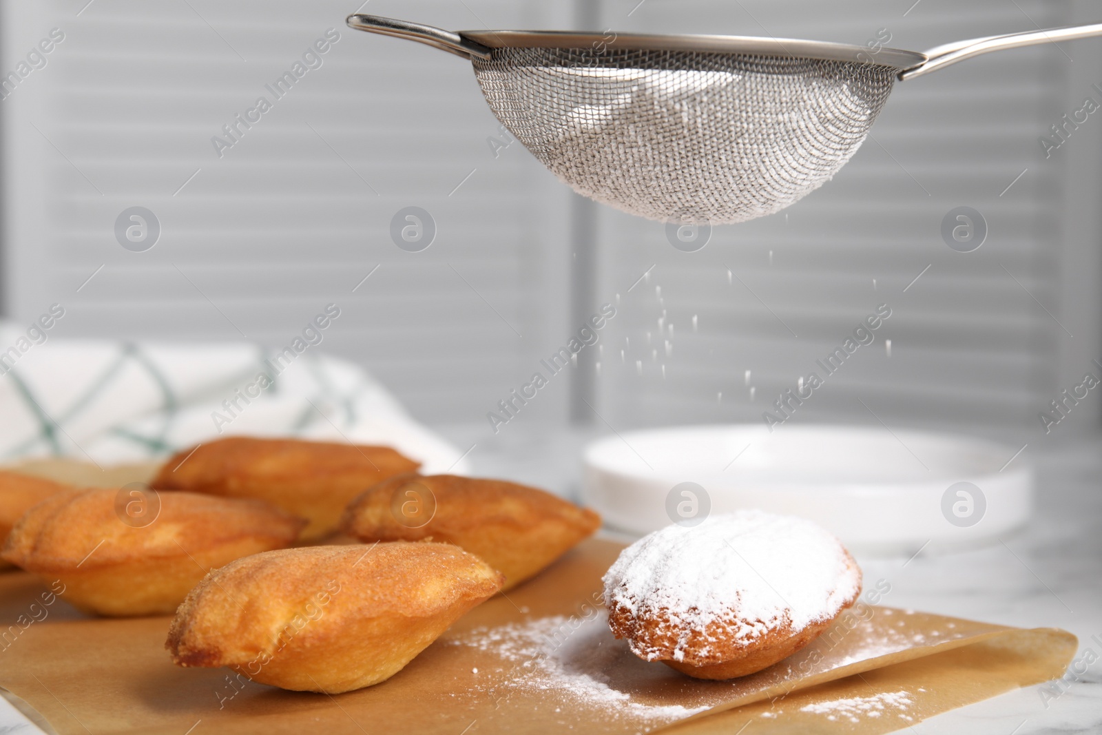 Photo of Decorating delicious madeleine cakes with powdered sugar on table, closeup