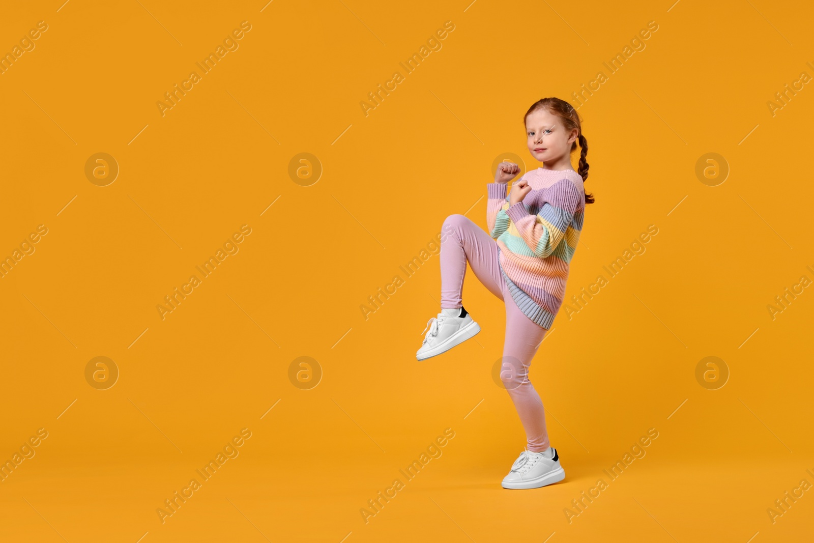 Photo of Cute little girl dancing on orange background, space for text