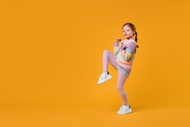 Cute little girl dancing on orange background, space for text