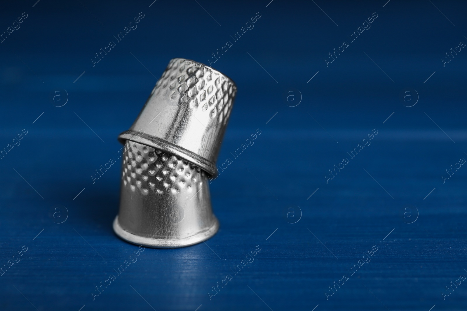Photo of Silver thimbles on blue wooden table, space for text. Sewing accessories