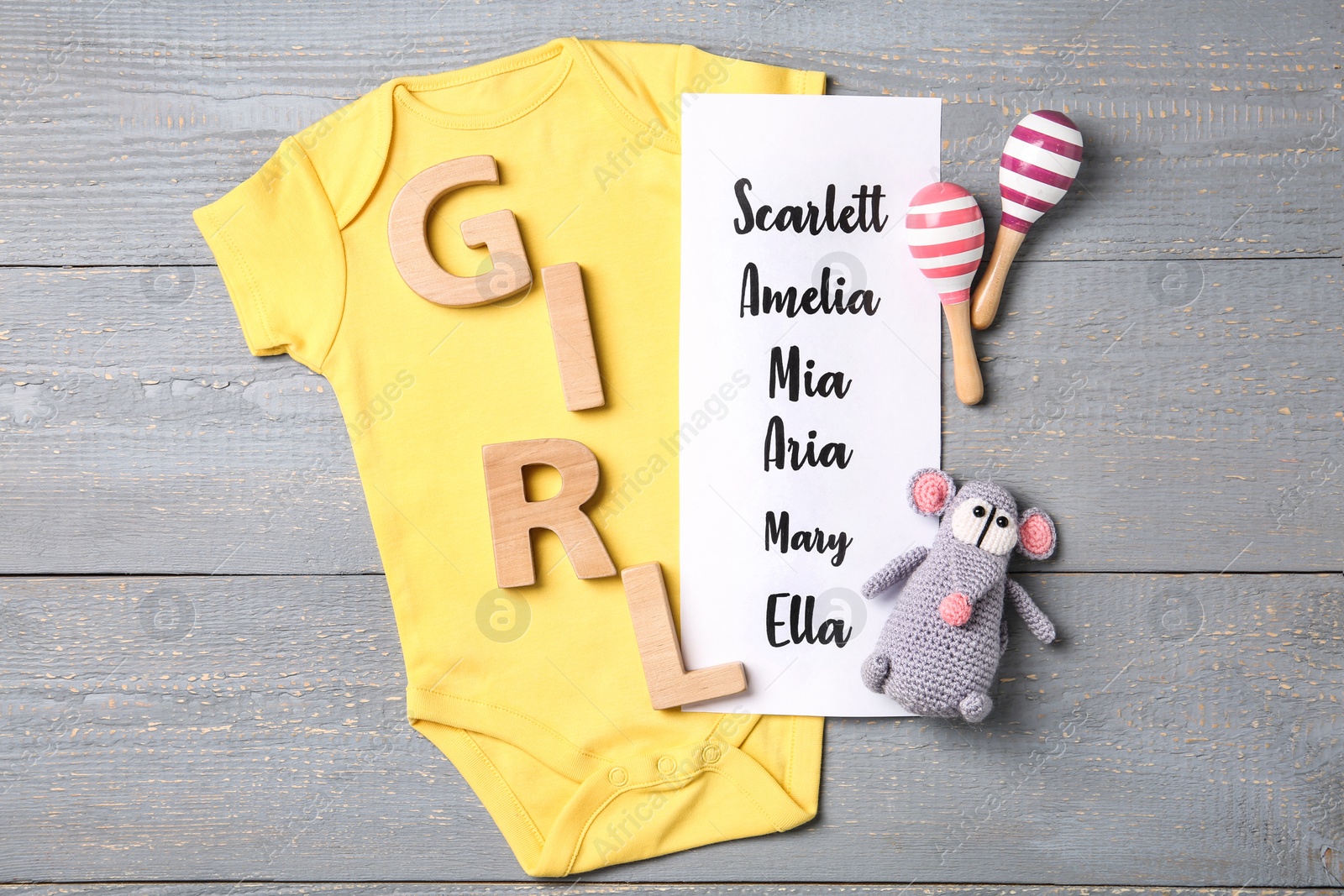 Photo of Bodysuit, list of baby names and toys on grey wooden background, flat lay