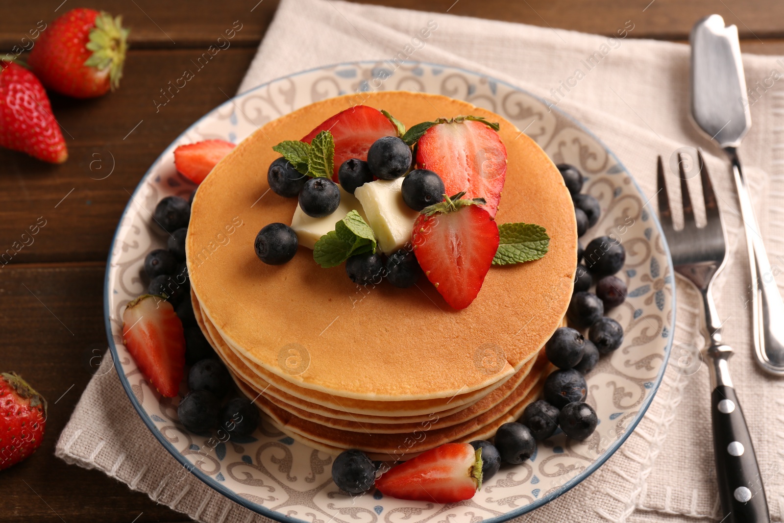 Photo of Delicious pancakes with fresh berries and butter served on wooden table, closeup