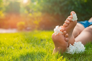 Teenage girl with beautiful hortensia flowers lying on green grass outdoors, closeup. Space for text