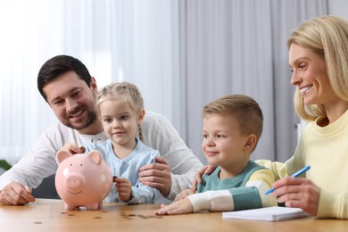 Photo of Planning budget together. Little girl with her family putting coins into piggybank indoors