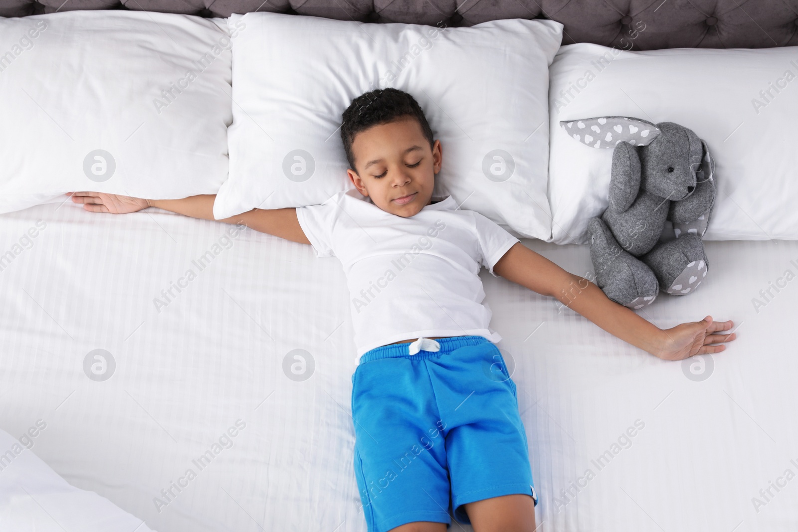 Photo of Cute little African-American boy with toy rabbit sleeping in bed, top view