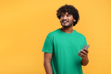 Handsome smiling man using smartphone on yellow background, space for text