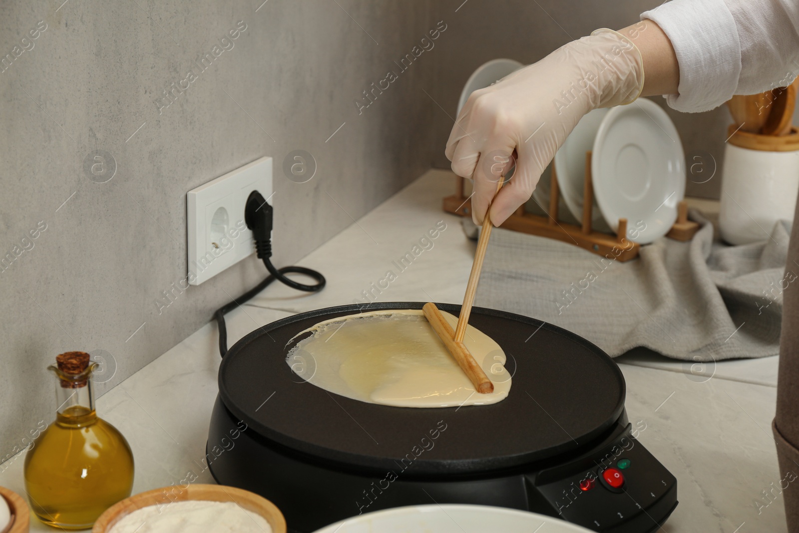 Photo of Woman cooking delicious crepe on electric pancake maker at white marble table in kitchen, closeup