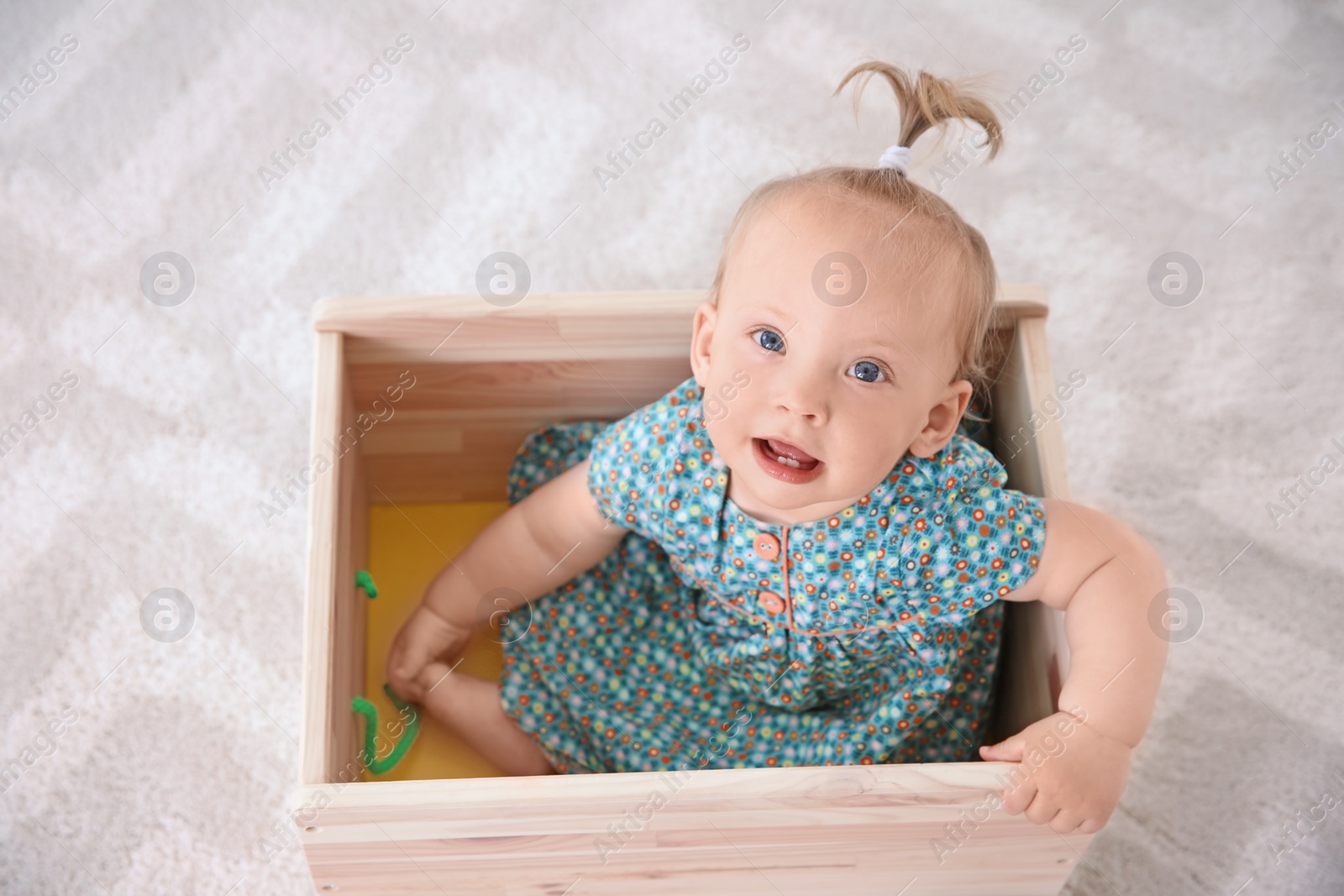 Photo of Adorable baby girl playing in wooden cart at home