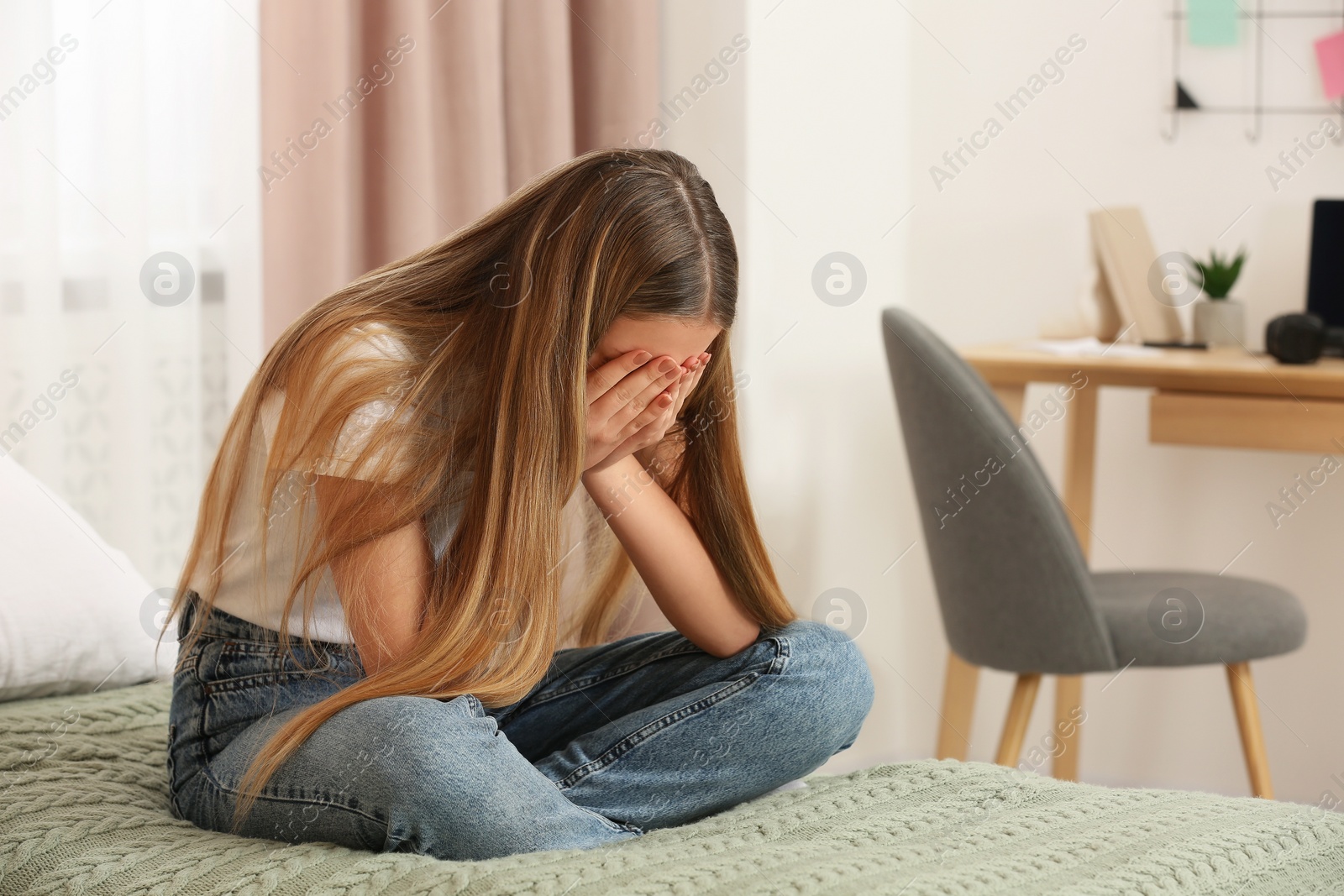 Photo of Unhappy teenage girl covering face with hands on bed at home