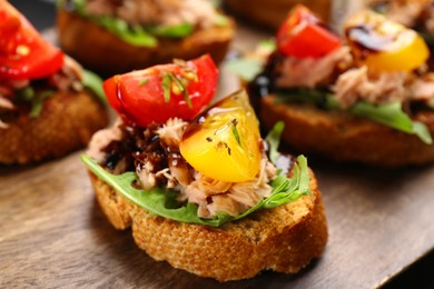 Photo of Delicious bruschettas with balsamic vinegar, tomatoes, arugula and tuna on wooden table, closeup