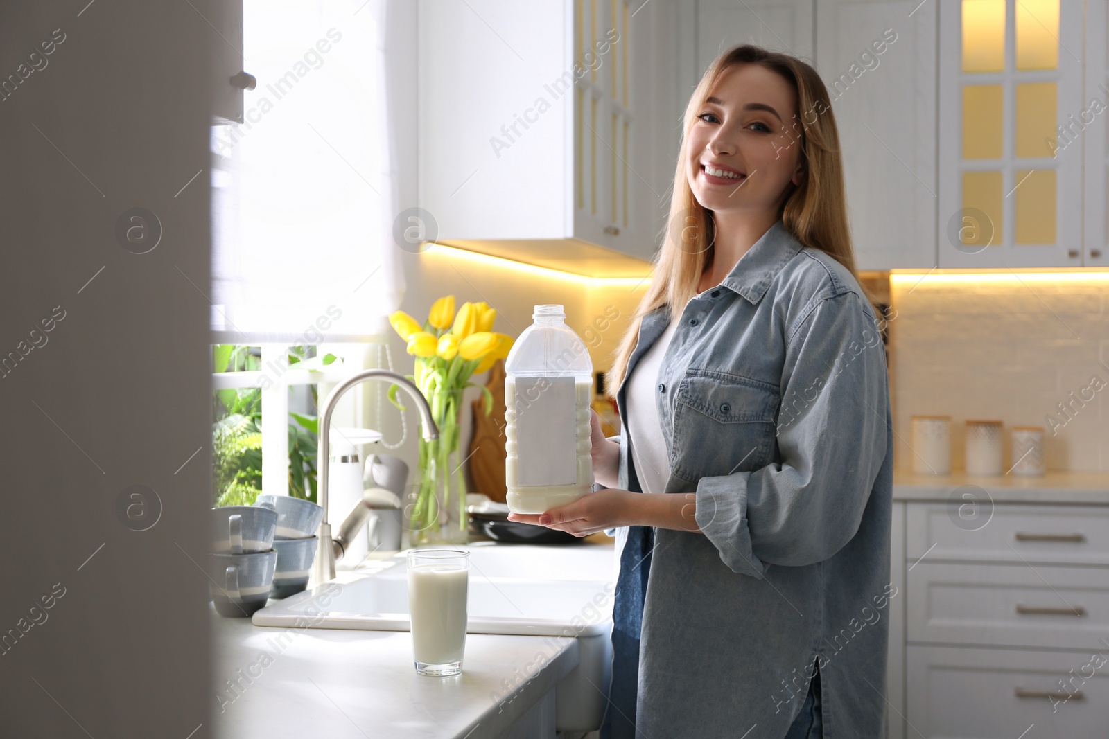 Photo of Young woman with gallon bottle of milk and glass at white countertop in kitchen